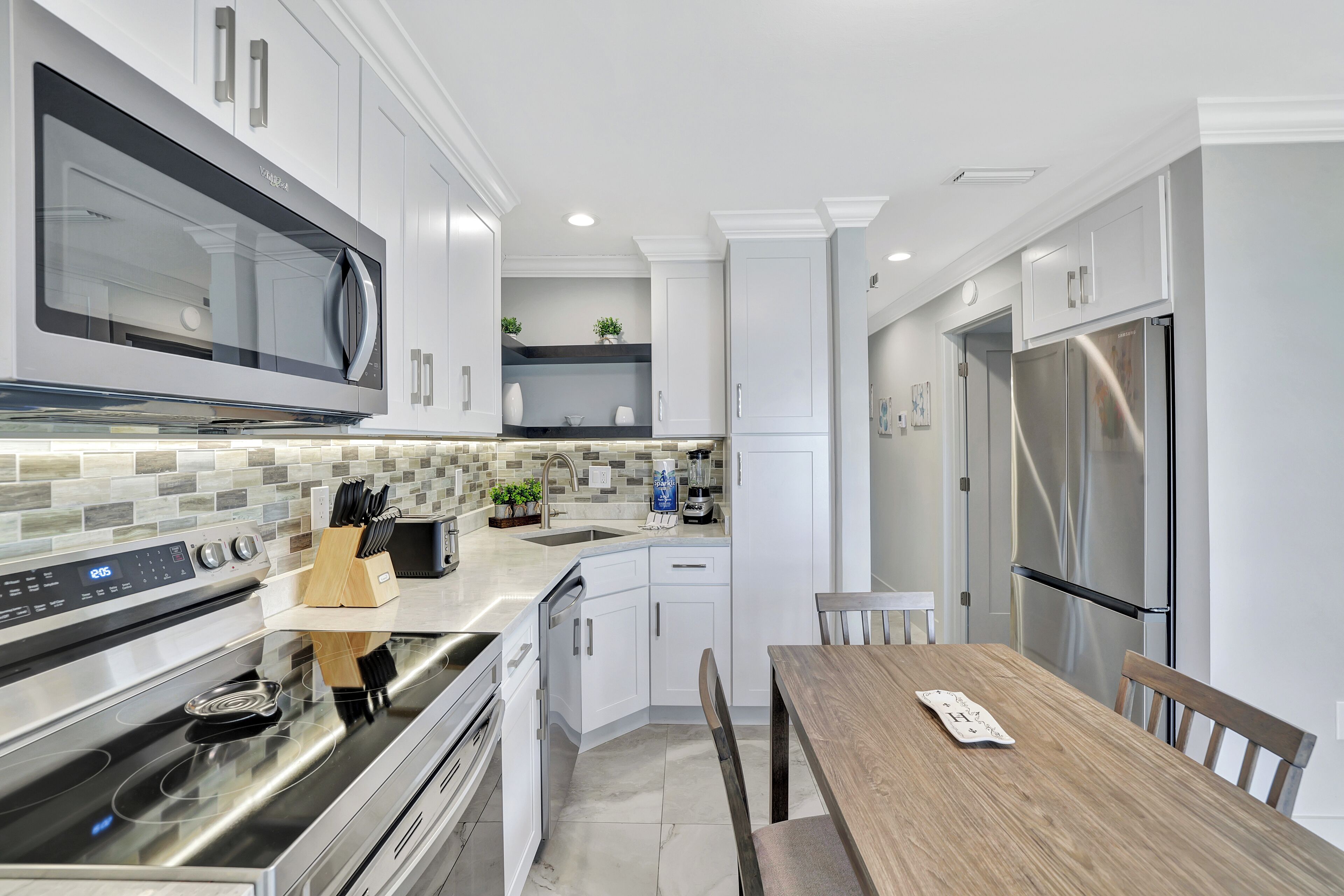 A modern kitchen with stainless steel appliances, white cabinetry, and a wooden dining table.