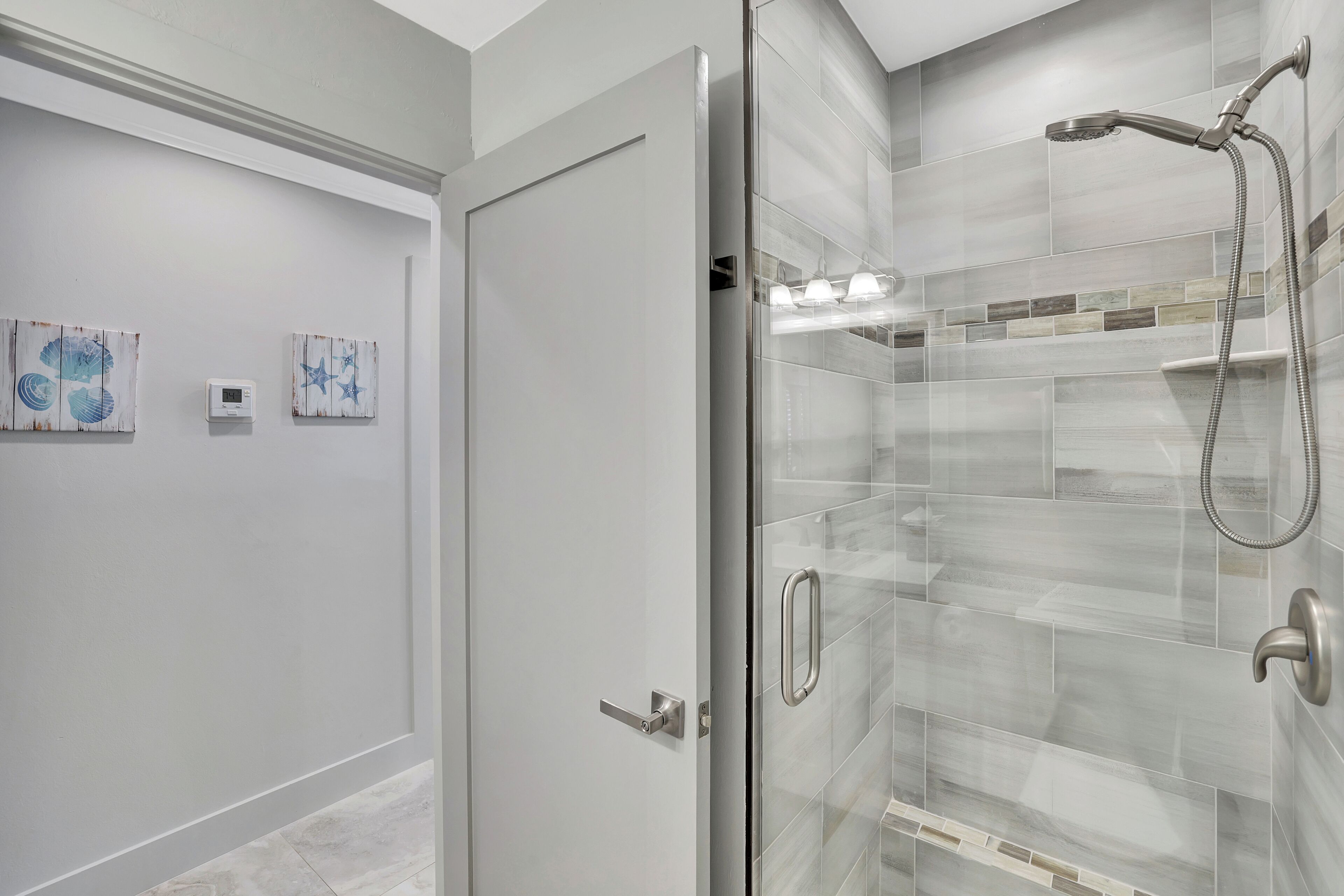 Une salle de bain moderne dotée d’une douche à parois de verre, d’une porte avec une poignée et de deux appliques murales.
