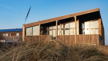 A wooden building with large windows and a balcony, surrounded by tall grass.