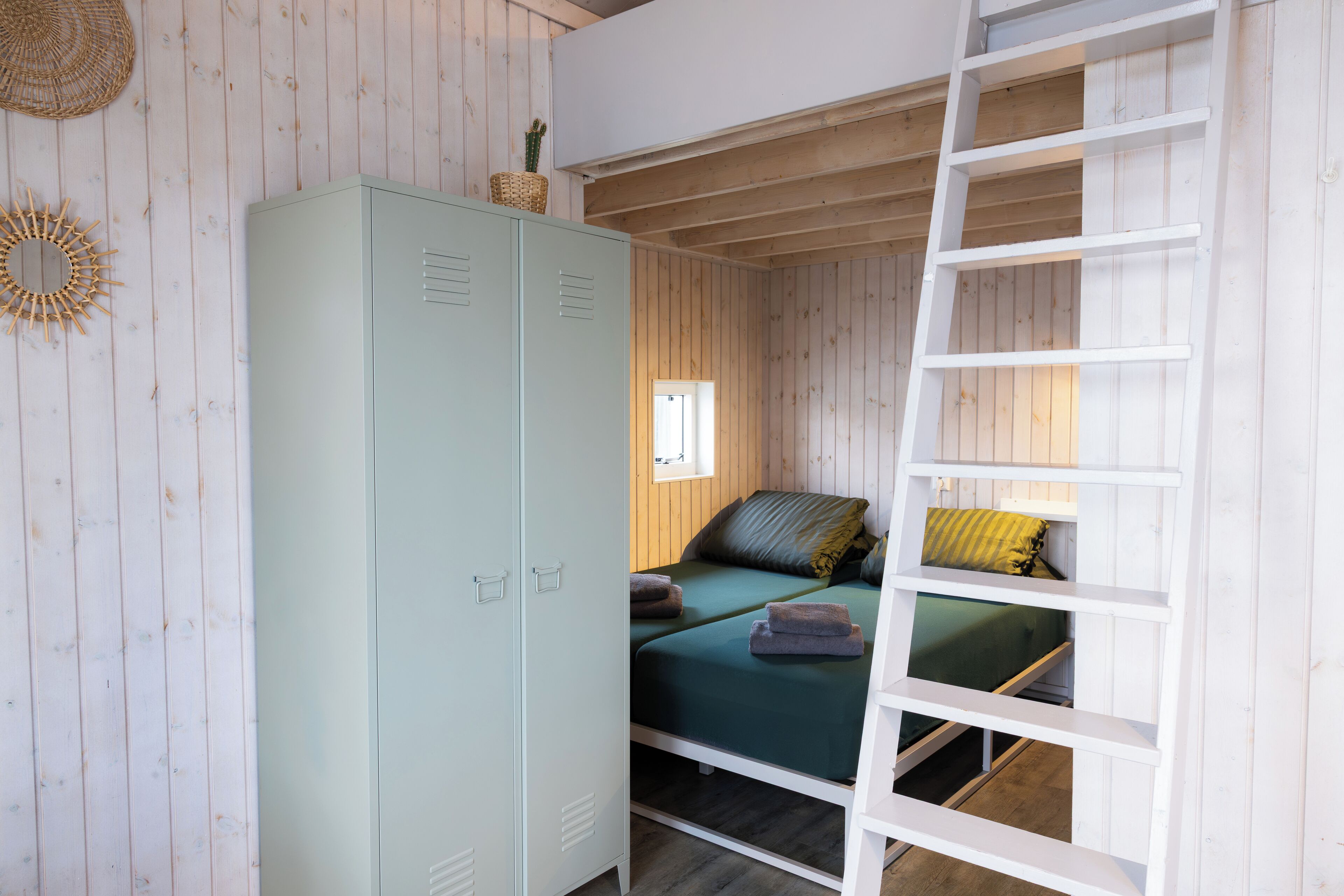A room with a bunk bed, a wardrobe, a ladder, and a window.