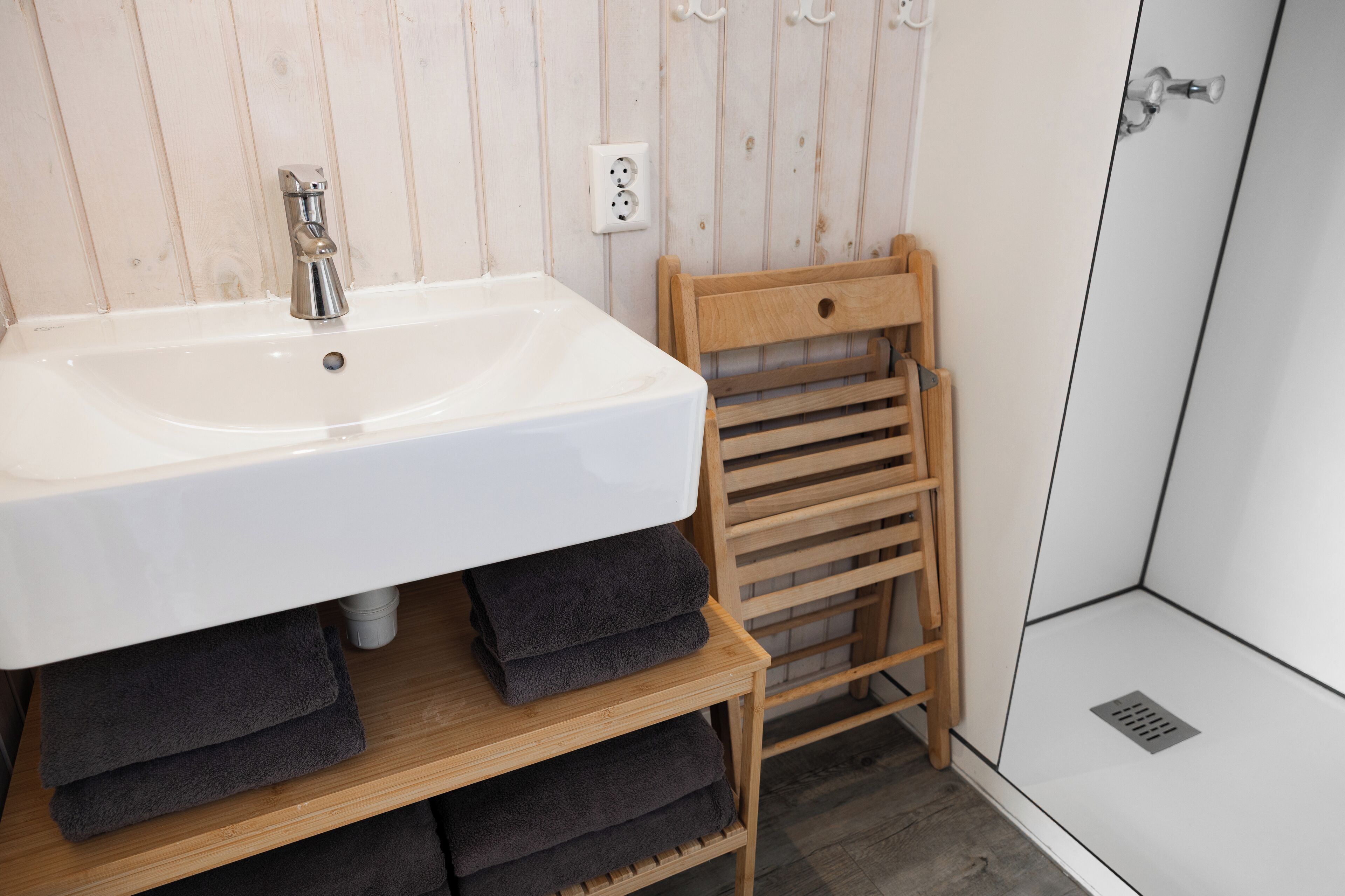 A bathroom with a white sink, wooden towel rack, and a shower area.