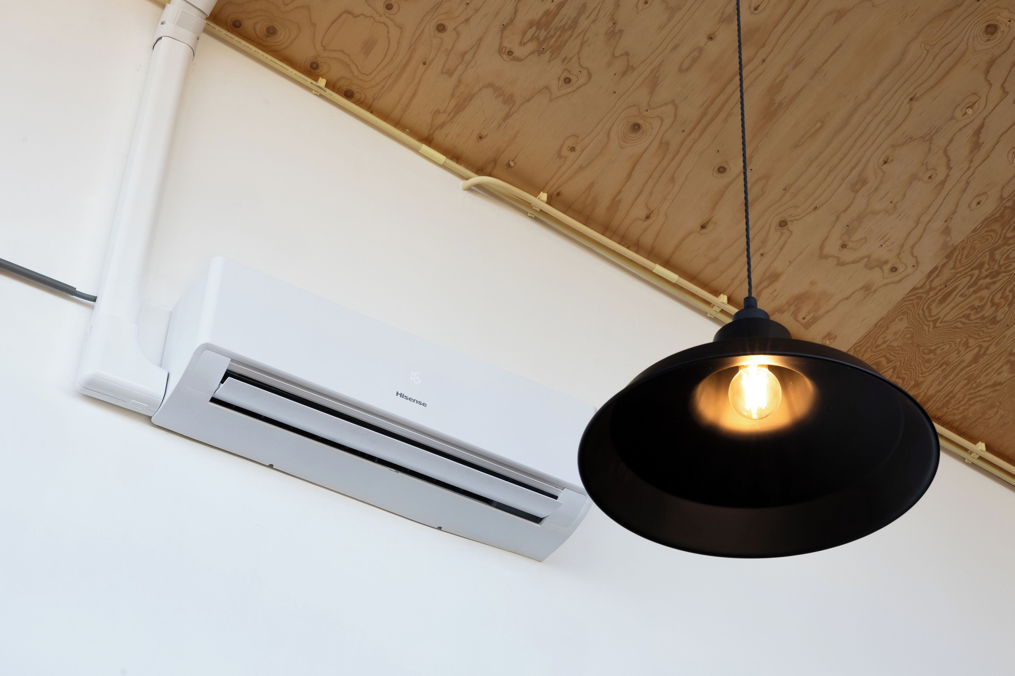 A white air conditioning unit mounted on a wall with a wooden ceiling.