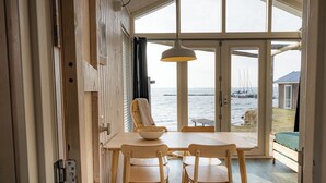 A wooden dining table with chairs, a hanging light fixture, and a view of the sea through large glass doors. - Brouwersdam Stay (Ouddorp)