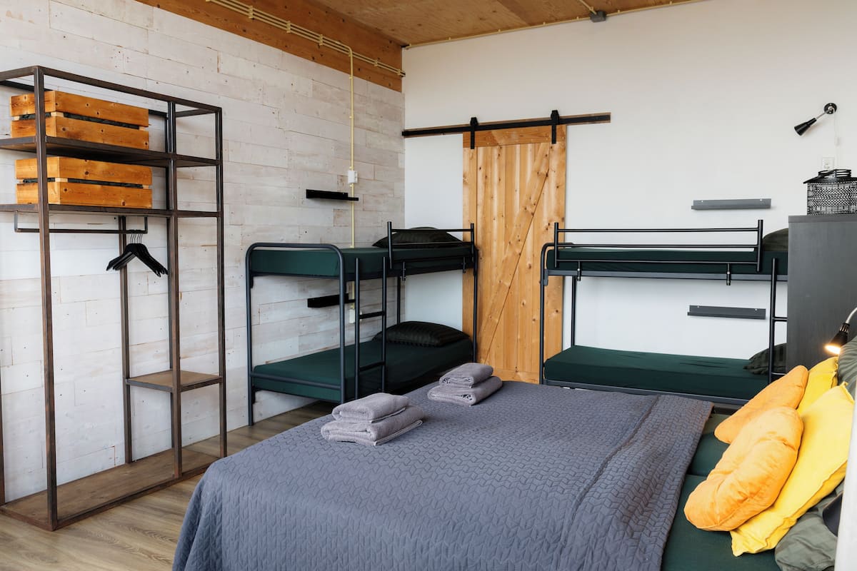 A dormitory room with bunk beds, a wardrobe with wooden crates, and a bed with pillows.