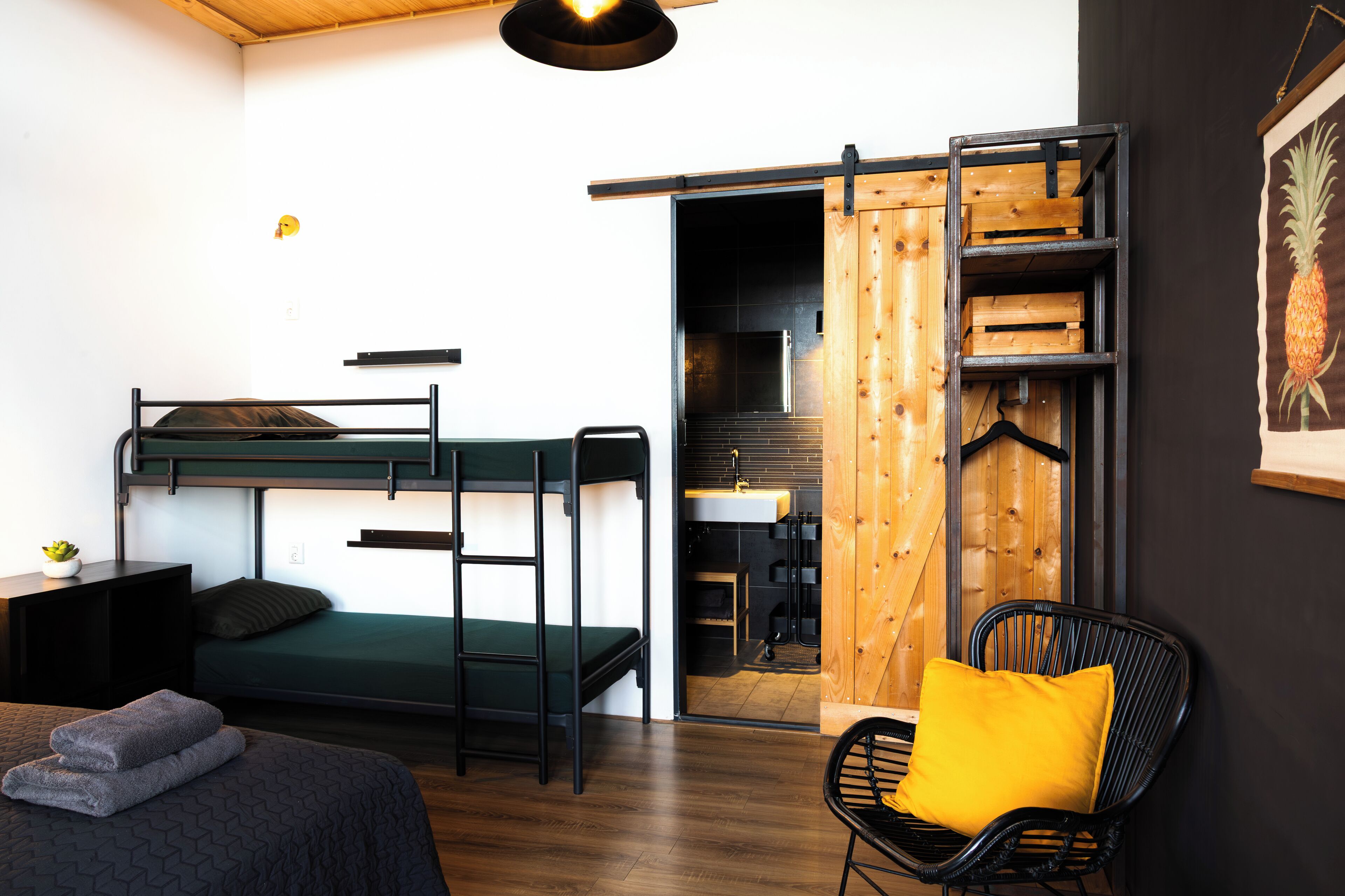 Un lit superposé avec un matelas vert, une échelle en métal noir, une petite table de chevet avec une plante et une chaise avec un coussin jaune.