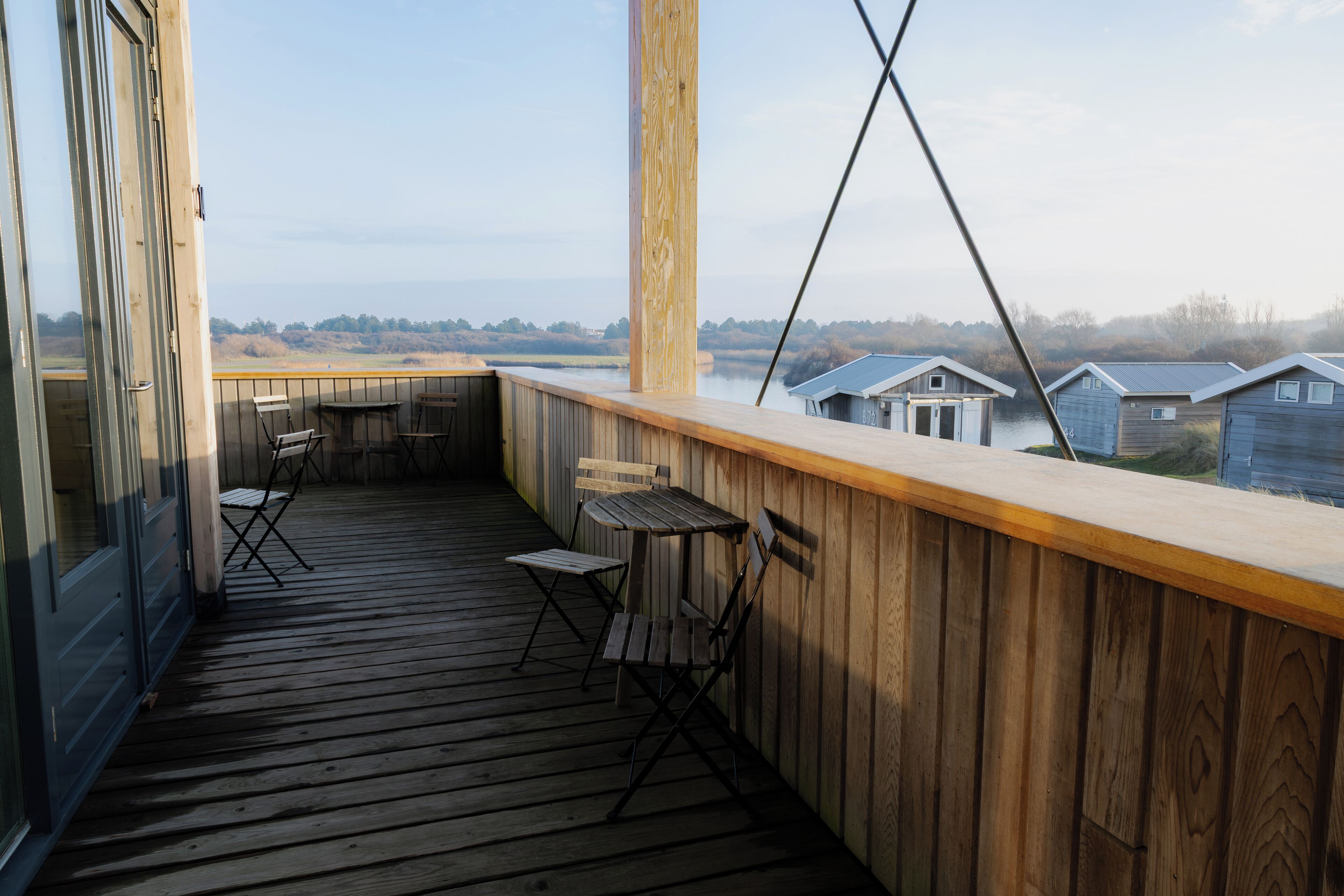 A wooden deck with a table and chairs, overlooking a body of water and houses.
