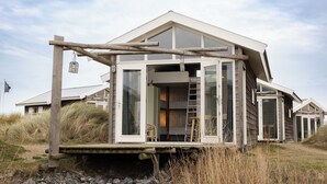 A modern house with large windows, a wooden deck, and a ladder leading to the entrance. - Brouwersdam Stay (Ouddorp)