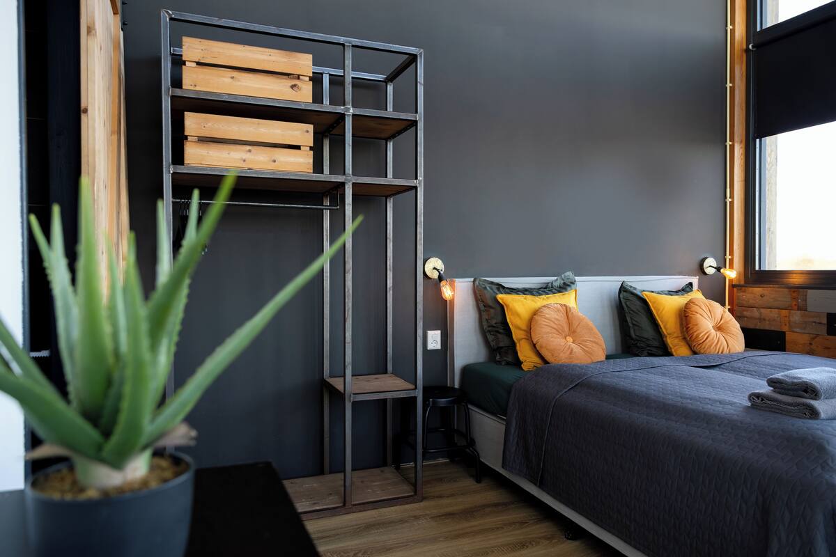 A bedroom with a bed, a wooden shelf unit, and a potted plant.