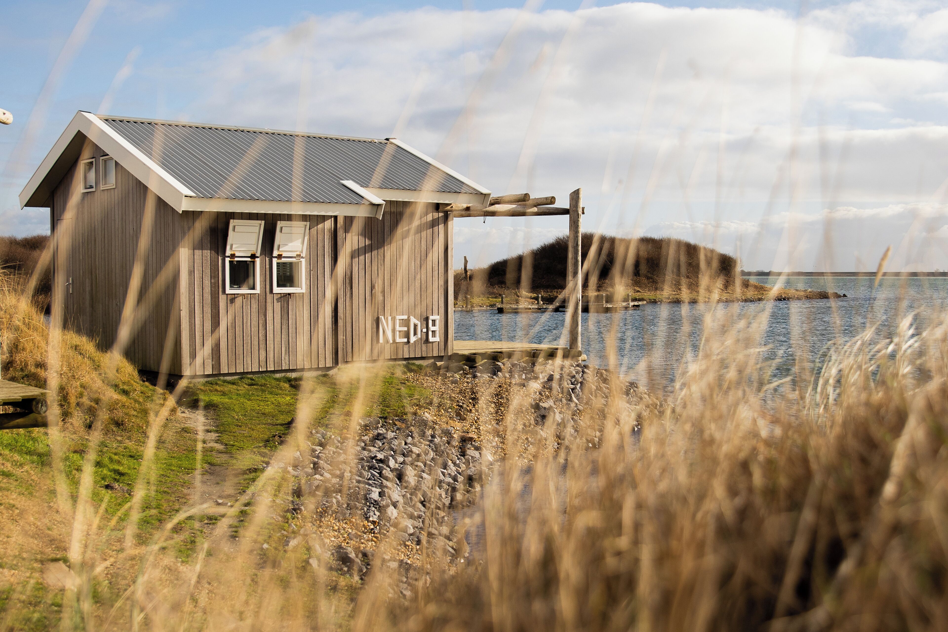 A wooden structure with a metal roof, labeled "NEDB," near a body of water.