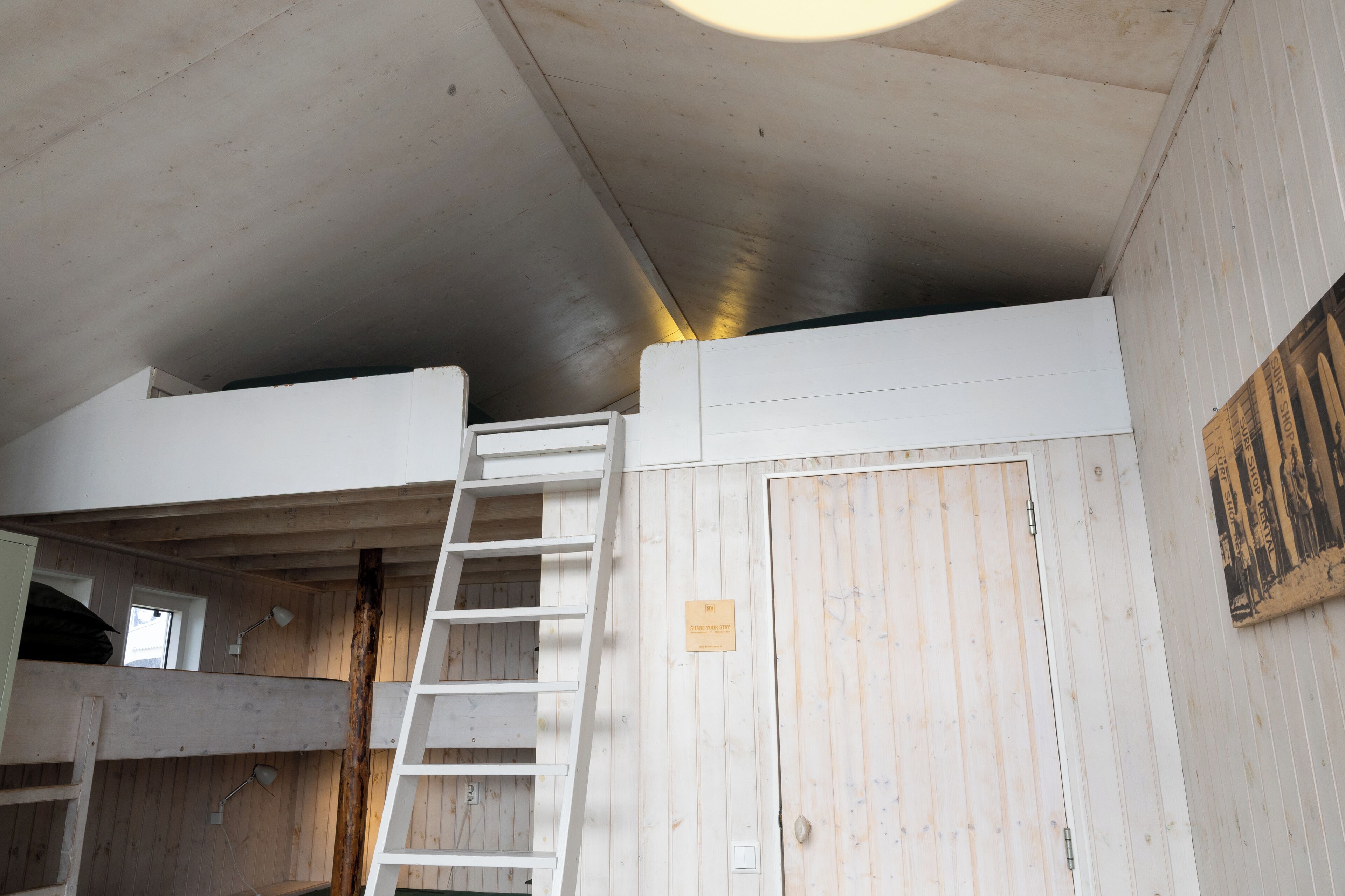 A room with a wooden floor, a white door, a ladder, and a small window.