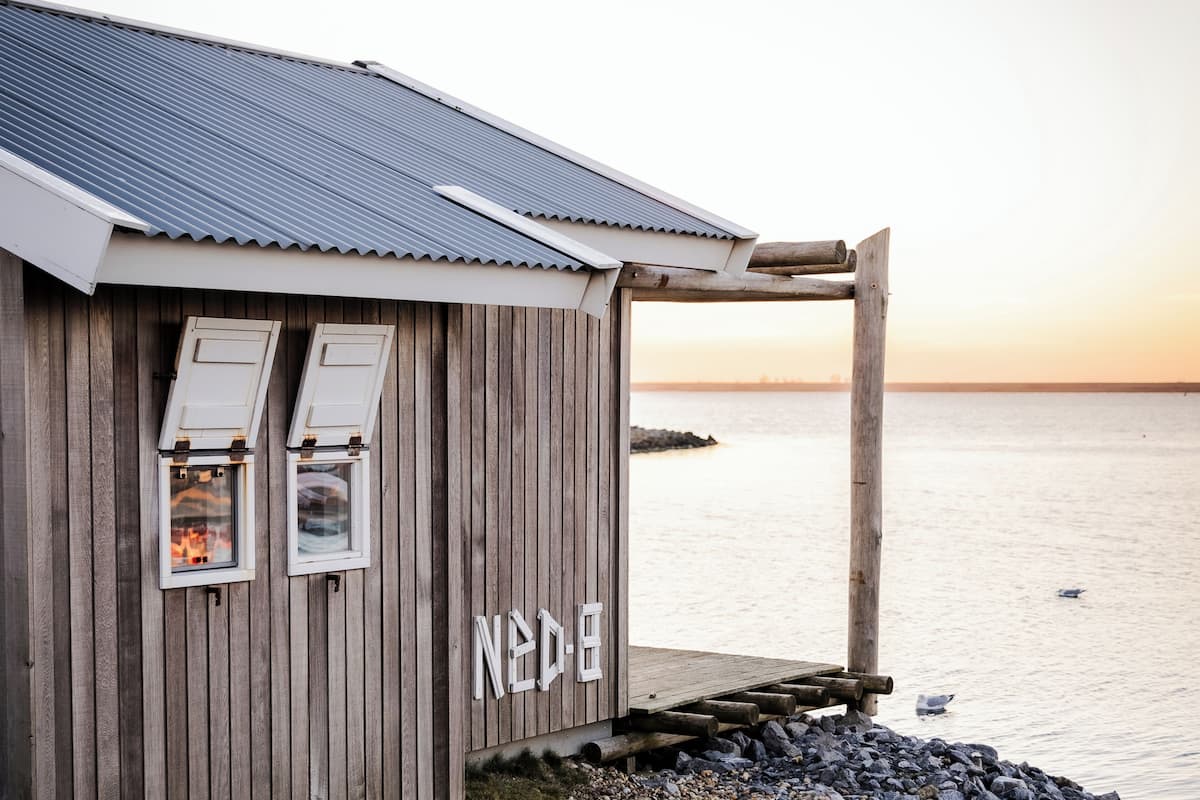 A wooden building with two windows and a sign reading "NED-E" near the water.