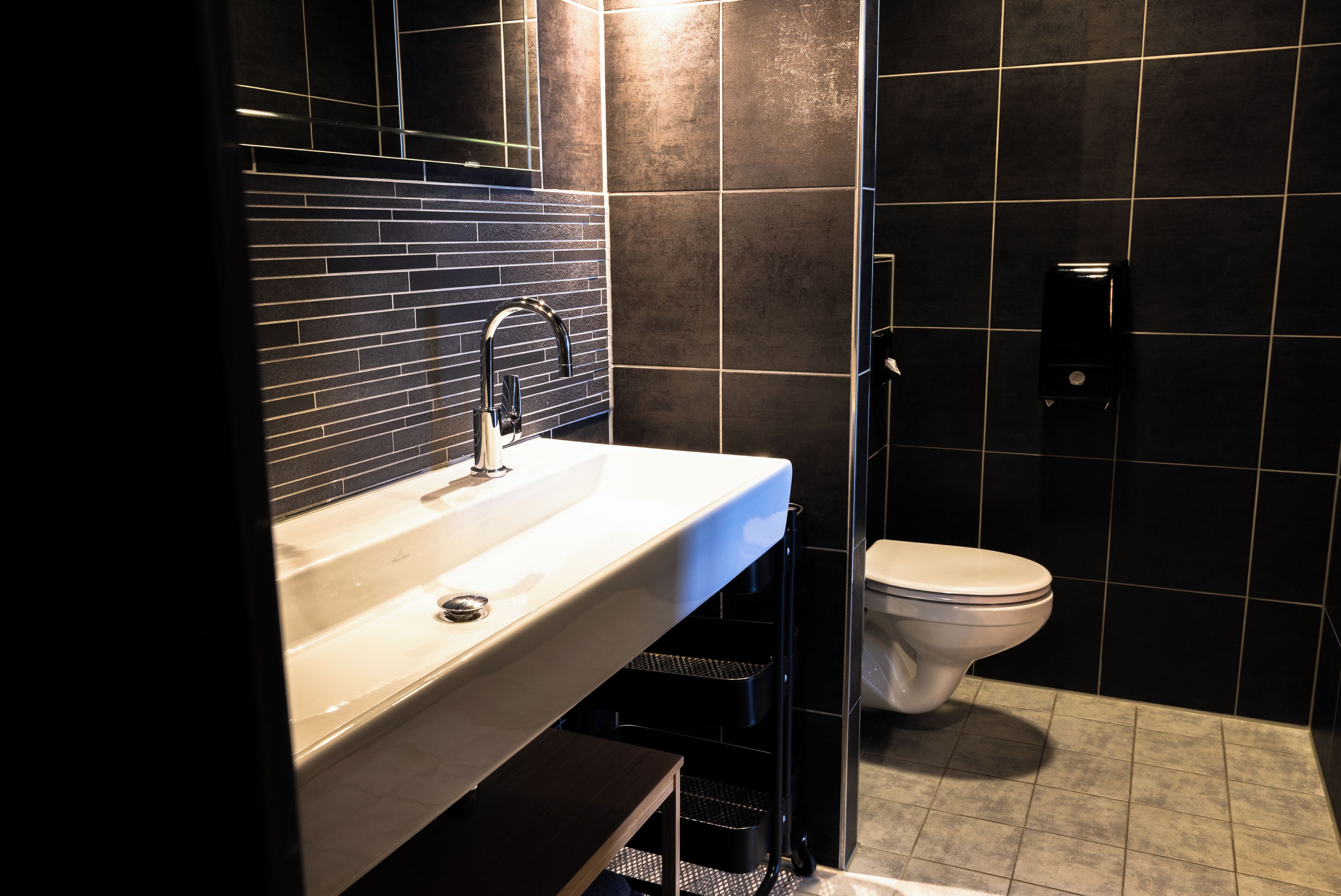 Un bagno moderno con un lavandino bianco, piastrelle nere e un water.