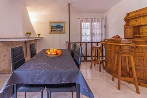 A dining area with a long table, chairs, a fruit bowl, a wooden cabinet, and a painting on the wall. - Vacation House Nuraghes (Pittulongu)