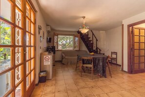 A spacious living area with a dining table, a sofa, and a staircase leading to an upper level. - Vacation House Nuraghes (Pittulongu)