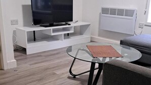 A modern living room with a flat-screen TV on a white entertainment unit, a glass coffee table, and a grey sofa. - Central Sheffield 1-Bed (Sheffield)