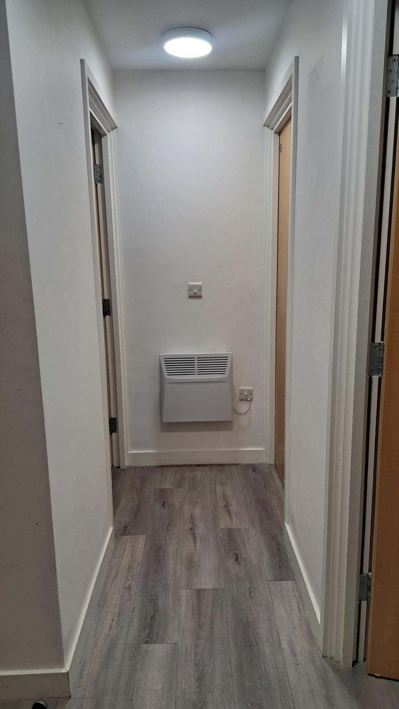 A narrow hallway with a white wall, a ceiling light, and a white air conditioning unit mounted on the wall.
