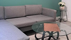 A modern living room with a grey sectional sofa, a glass coffee table with a woven placemat, and a cityscape painting on the teal wall. - Central Sheffield 1-Bed (Sheffield)