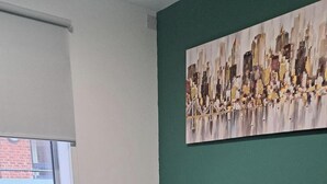 A modern living room with a grey sectional sofa, a glass coffee table, and a cityscape painting on the wall. - Central Sheffield 1-Bed (Sheffield)