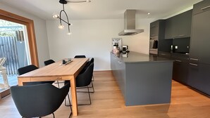 Eine moderne Küche mit einer zentralen Kochinsel, dunklen Schränken und einem Essbereich mit Holztisch und schwarzen Stühlen.