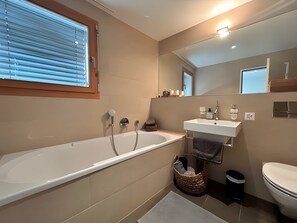 Ein modernes Badezimmer mit einer Badewanne, einem Waschbecken, einer Toilette und einem Fenster.