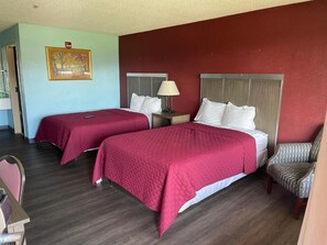 A hotel room with two beds, a chair, a nightstand, and a framed picture on the wall.