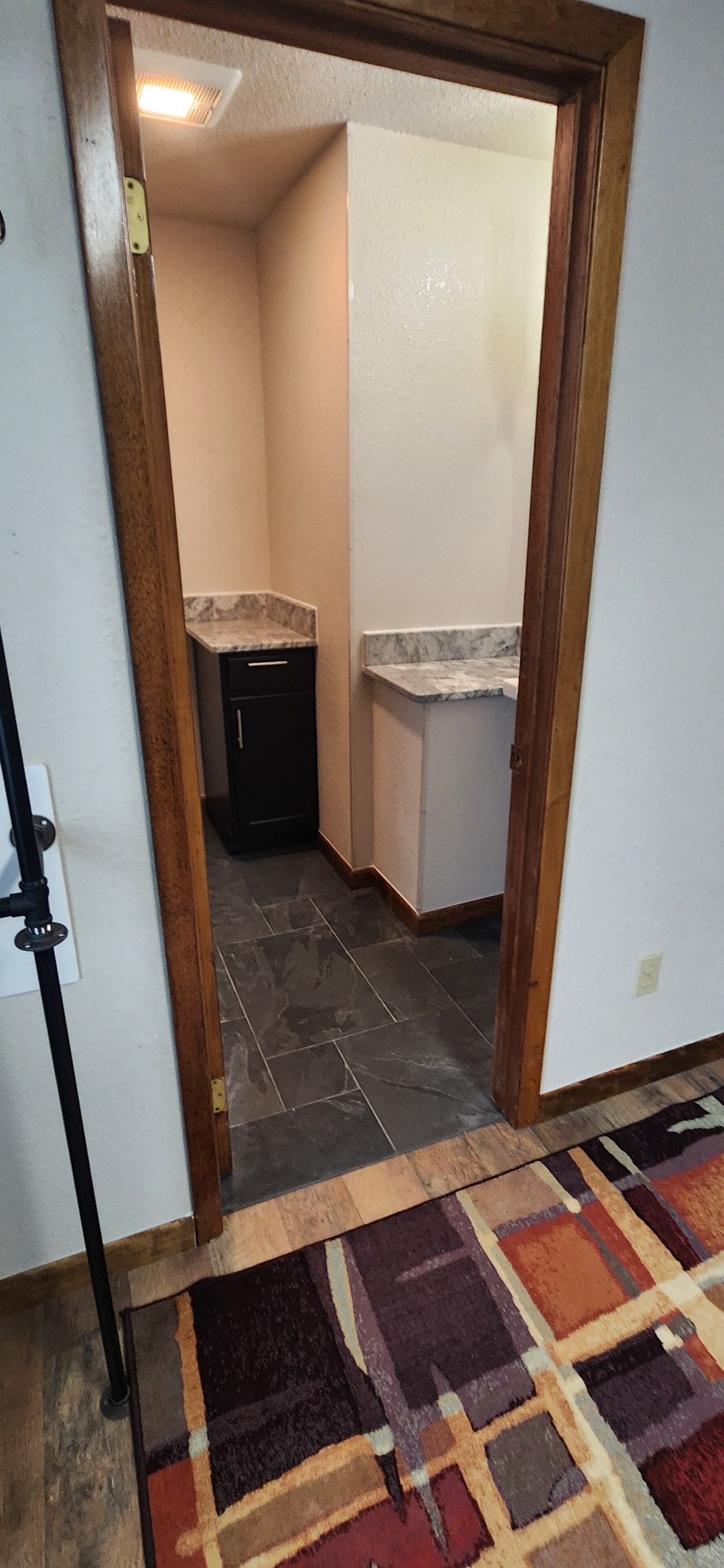 A hallway leading to a kitchen with dark tiled flooring and a patterned rug.