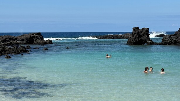 A clear turquoise sea with rocky formations and three people swimming. - Hilton Waikoloa Pool Pass 2026-27, Beach and Baby Gear! (Waikoloa Village)