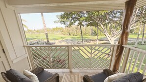 Ein Balkon mit Korbmöbeln, einem Holztisch und Blick auf einen Golfplatz.