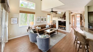 A spacious living room with a large sofa, two armchairs, a coffee table, and a TV. There are multiple windows providing natural light and a view of the outdoors. - Hilton Waikoloa Pool Pass 2026-27, Beach and Baby Gear! (Waikoloa Village)