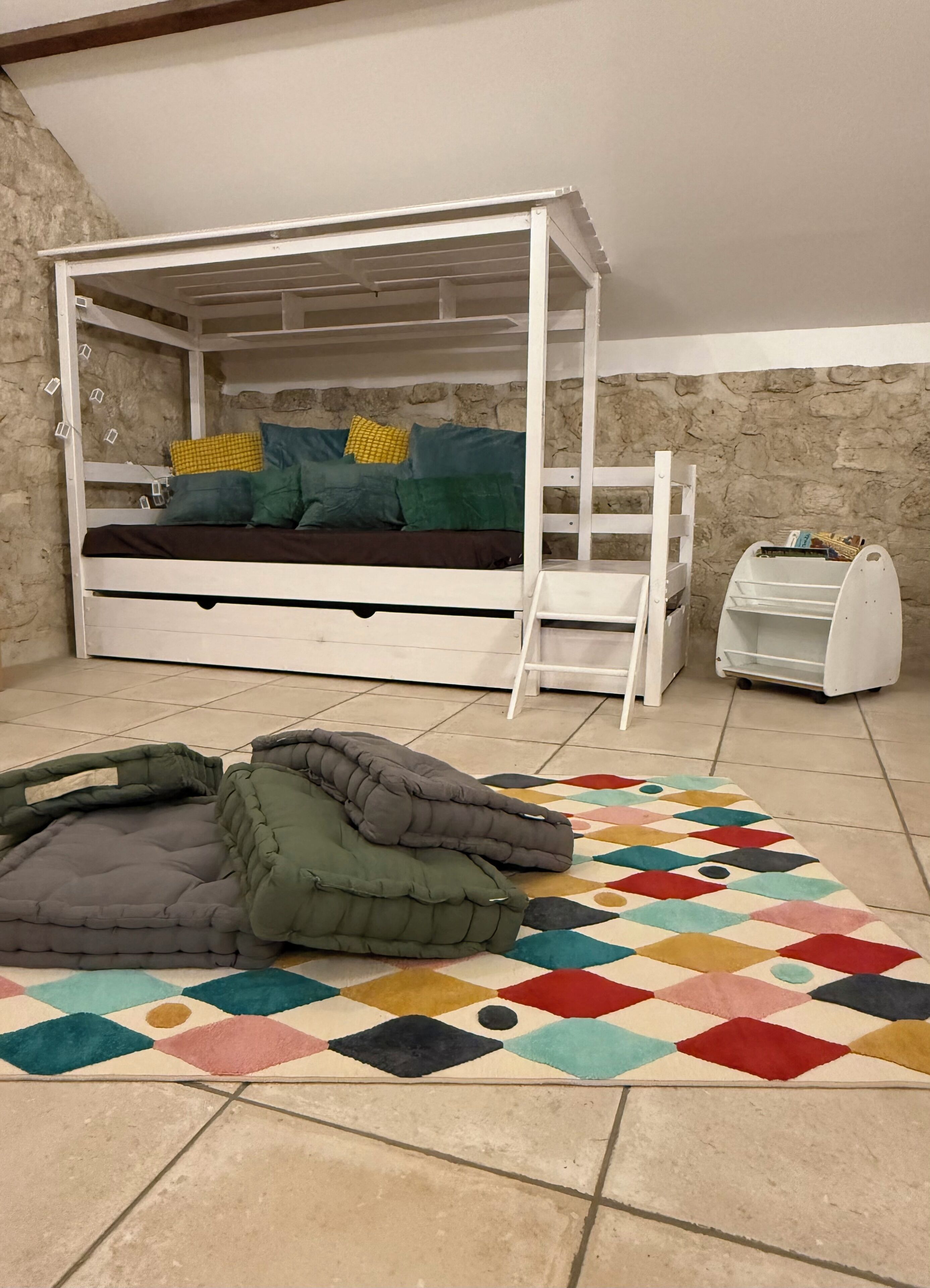 Ein Stockbett mit einer Leiter, einem Stauraum und einem bunten Teppich auf Fliesen.
