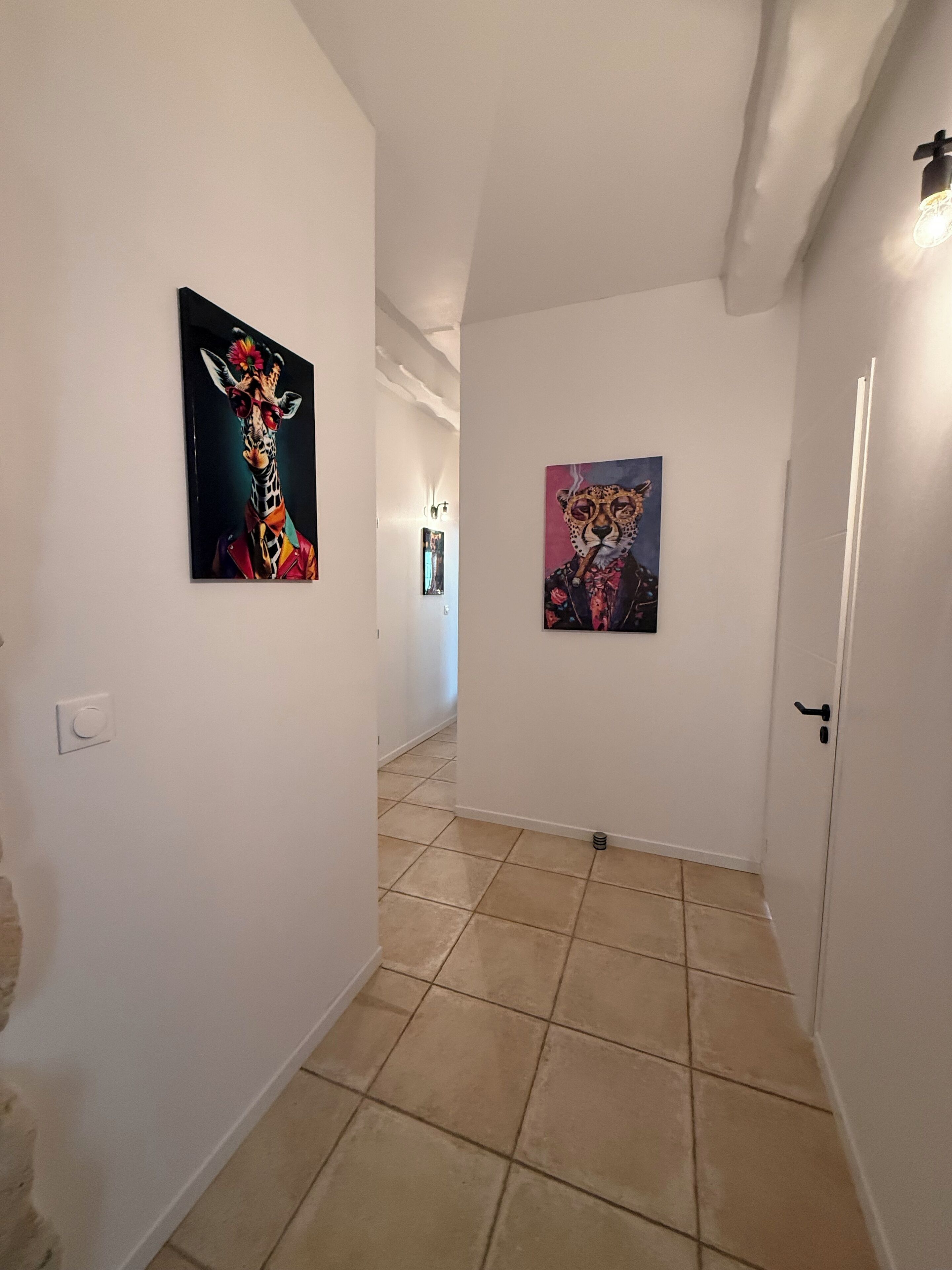 A hallway with two paintings on the walls, a tiled floor, and a door at the end.