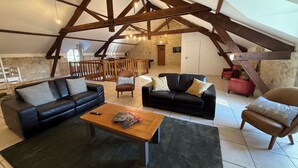 En rummelig, loft-inspireret opholdsstue med synlige træbjælker, en sort lædersofa, et træbord og en stenvæg.