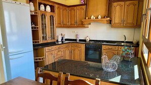 Une cuisine avec des meubles de rangement en bois, un plan de travail en granit, un réfrigérateur et une table à manger avec des chaises.
