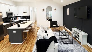 Een moderne keuken met witte kasten, een centraal eiland en een eethoek met houten vloer.