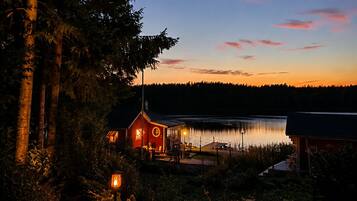 A lakeside cabin with a dock, surrounded by trees and a clear sky.
