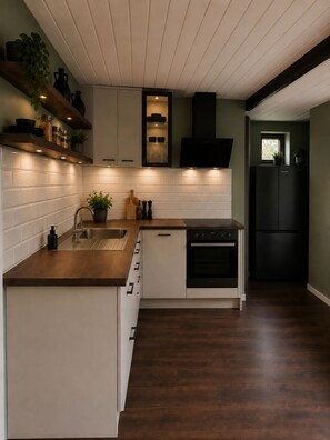 Une cuisine moderne avec des meubles blancs, un plan de travail en bois, un four encastré et un réfrigérateur noir.