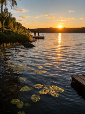 A calm lake at sunset with a dock and two people fishing. - A Stunning Swedish House by the Lake • Fireplace, Boat & Separate Guest House (Belganet)