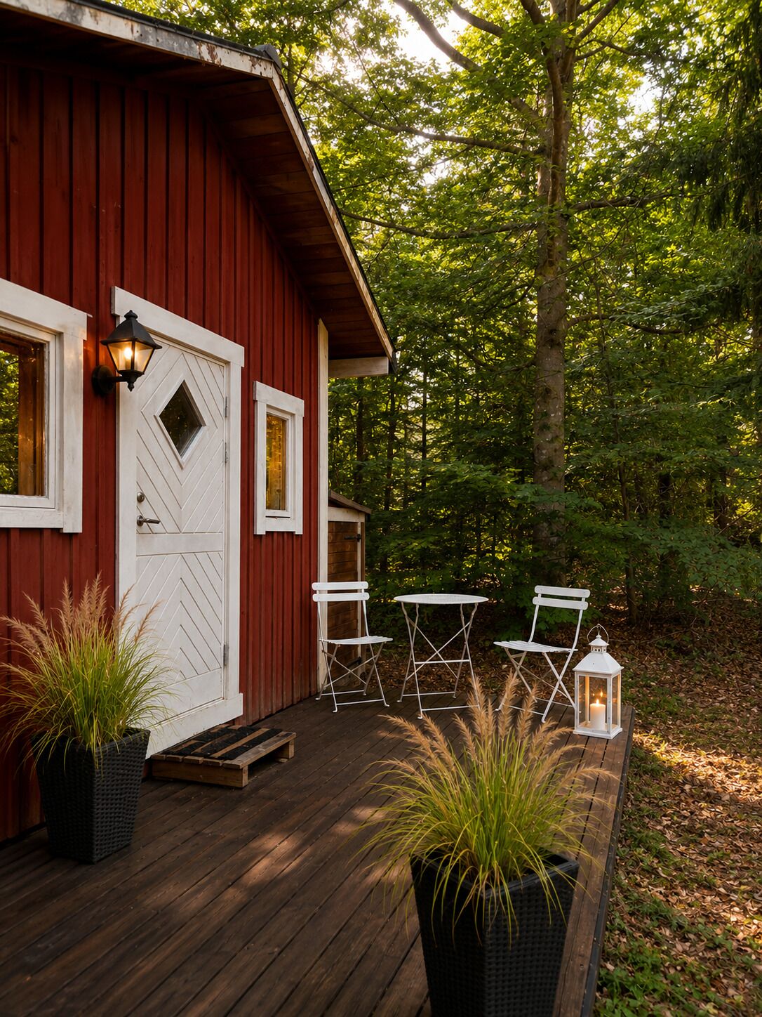 A red wooden cabin with a white door, two windows, and a porch with a table and chairs.