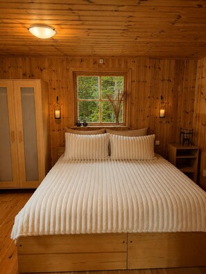 A wooden room with a bed, a window, and two wall-mounted lamps. - Swedish Magic – An Exclusive Retreat by the Lake with a Private Dock, Boat, and Guest House (Belganet)