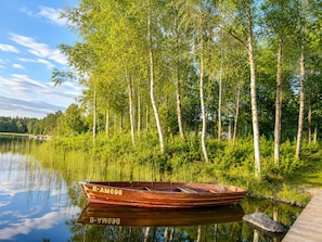 Een houten boot met registratienummer B-AM698 en B-YWEA8 afgemeerd aan een rustig meer, omringd door bomen.