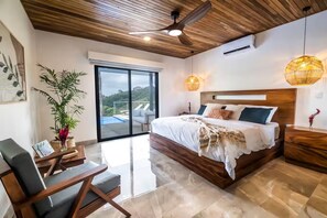 Ein modernes Schlafzimmer mit einem großen Bett, Holzboden und Blick auf einen Swimmingpool.