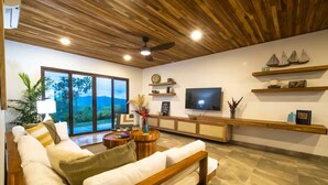 Ein modernes Wohnzimmer mit Holzboden, einem großen Fernseher und Blick ins Freie.
