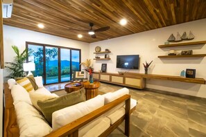 Ein modernes Wohnzimmer mit Holzboden, einem großen Fernseher und Blick ins Freie.