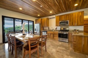 Eine moderne Küche mit Holzschränken, Edelstahlgeräten und einem Essbereich mit großem Tisch und Stühlen.