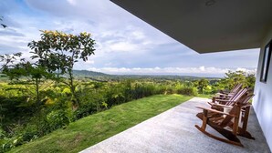 Ein Balkon mit Betonboden und Holzschaukelstühlen, der auf eine üppige, grüne Landschaft mit Bergen in der Ferne blickt.
