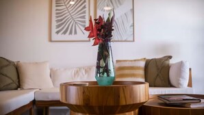 Ein Wohnzimmer mit einem runden Holztisch, einer klaren Glasvase mit Blumen und einem weißen Sofa mit gestreiften Kissen.