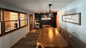 A dining area with a long wooden table, chairs, a chandelier, and a wall-mounted sign.