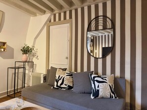 Ein modernes Wohnzimmer mit grauem Sofa, Streifen-Tapete, einem runden Spiegel, einem Blumentopf und einer Heizung.