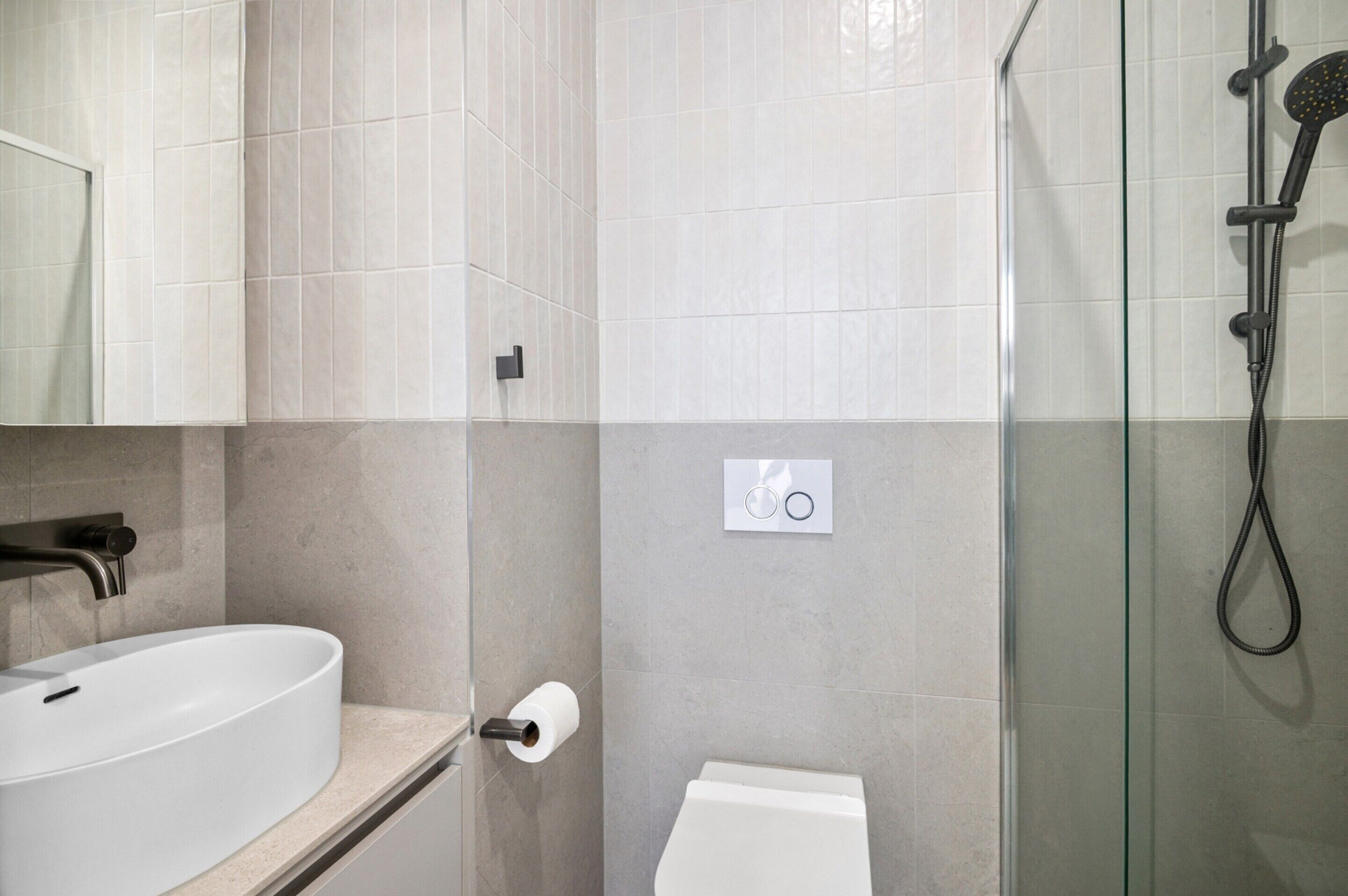 Et moderne badeværelse med hvid vask, toilet og glasvægs-brusekabine.