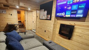 A cozy room with a large sectional sofa, a flat-screen TV mounted on the wall, and a fireplace. - Cozy 1-bedroom bunk style apartment Game Rm/Gym/Stream in historic McDowell! (McDowell)